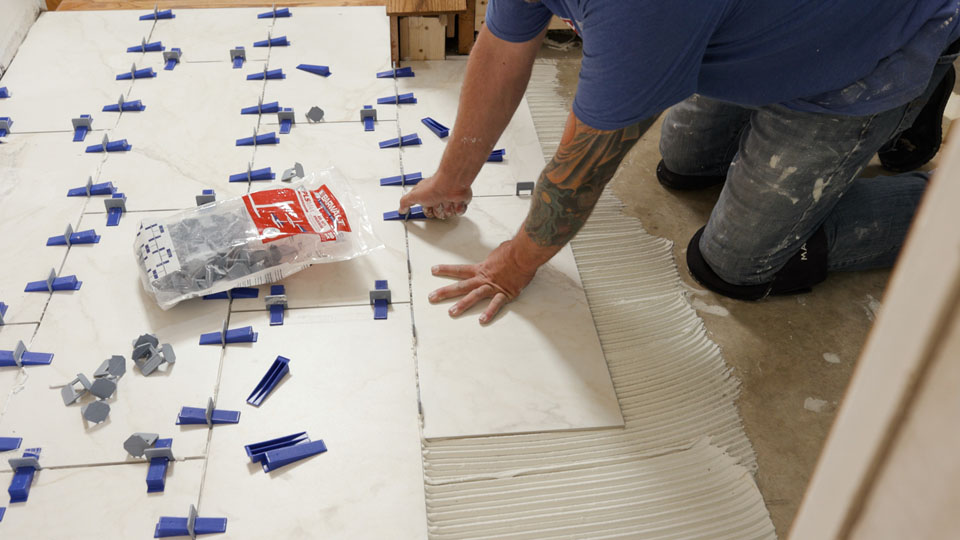 Person installing large marble tiles using spacers on a floor, with tile setting tools nearby.